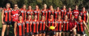 Blackburn inaugural team 2018. 21 women in formation outside, red & black uniforms, coach kneeling in front row.